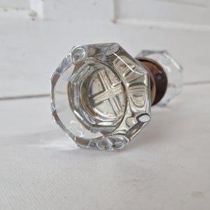 May include: Clear, octagonal glass doorknob with a brass base. The knob has a faceted design, reflecting light. The antique-style hardware is suitable for interior doors.