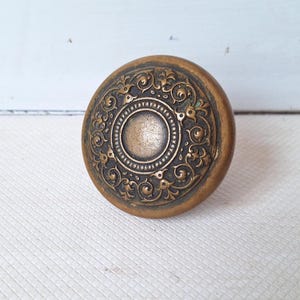 May include: Antique brass door knob with intricate floral and scrollwork detailing. The round knob features a central circular design surrounded by ornate patterns. The aged finish gives it a vintage aesthetic, perfect for adding character to any door.