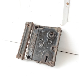 May include: Antique black metal door lock with intricate floral designs and a keyhole. The lock has a brass plate with the inscription "Russell & Co."