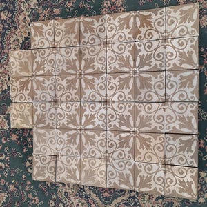 May include: A set of 25 brown ceramic tiles with a white floral pattern. The tiles are arranged in a grid pattern.
