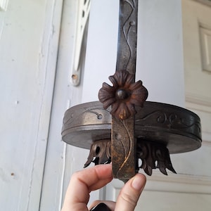 K&ouml;nnte beinhalten: Antike H&auml;ngeleuchte mit einem Schirm aus Milchglas. Die Leuchte hat einen dunklen Metallrahmen mit floralen und Ranken Details. Der handgehaltene Teil ist dunkel gef&auml;rbt. Die Leuchte ist auf einer wei&szlig;en Oberfl&auml;che montiert.