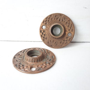 May include: Two antique brass door knobs with intricate geometric designs. The knobs have a circular shape with a central hole for a door handle.