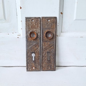 May include: A pair of antique door plates with intricate designs and a keyhole. The plates are made of metal and have a rusty patina.