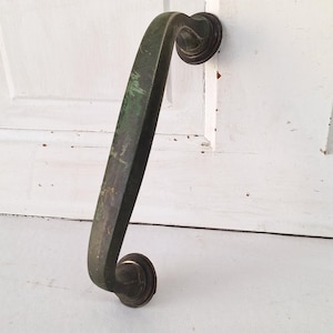 May include: An antique bronze door pull with a curved handle and decorative circular ends. The handle shows signs of age with a green patina. Two screws are included.