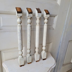 May include: Four white painted wooden balusters with brown wood tops. The balusters are arranged in a row on a white table.