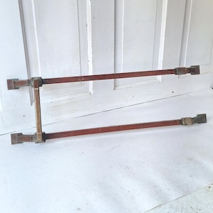 May include: Two-piece, rectangular, antique-style metal hardware. The horizontal bars are a reddish-brown color, connected by vertical bars and corner pieces. The hardware appears to be made of metal with a vintage aesthetic.