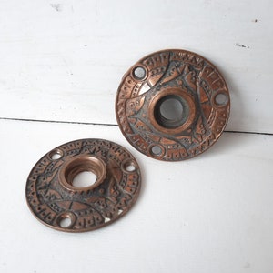 May include: Two antique copper door knob escutcheons with intricate geometric designs.