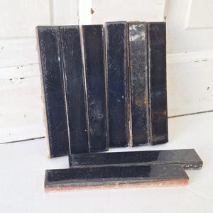 May include: A collection of rectangular, black tiles with a glossy finish. The tiles are arranged in vertical and horizontal stacks, revealing a rough, textured underside. The tiles vary in size and show signs of wear.