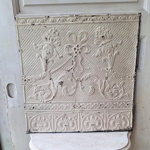 May include: White tin ceiling tile with an embossed floral design. The tile has a distressed look with some of the white paint chipped away.
