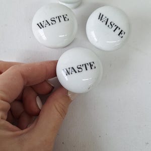 May include: Four white ceramic knobs with the word "WASTE" printed in black lettering.