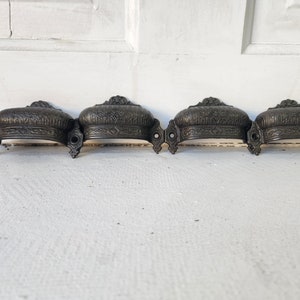 May include: Four antique-style black metal drawer pulls with ornate designs. Each pull has a curved shape and decorative details.