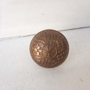 May include: A brass door knob with an intricate, embossed design featuring a central flower motif and geometric patterns.