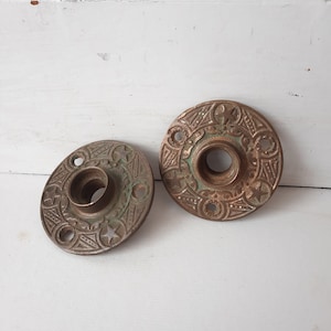 May include: Two antique brass door knobs with intricate star and floral designs. The knobs have a circular shape and a hole in the center for a door handle.
