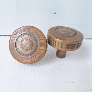 May include: Two antique brass door knobs with a decorative floral design. The knobs have a round shape and a raised edge.