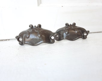 May include: Two antique-style cast iron drawer pulls with a decorative floral design. The pulls are a dark brown colour and have a slightly distressed finish.
