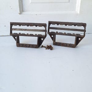 May include: Two antique cast iron drawer pulls with a grid pattern and the word "SHERER" embossed on the bottom. The pulls are rusty brown and have a worn finish.