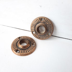 May include: Two antique brass door knob escutcheons with a decorative, concentric circle design.