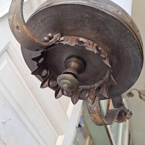 K&ouml;nnte beinhalten: Antike bronzefarbene H&auml;ngelampe mit wei&szlig;em Glasschirm. Die Leuchte verf&uuml;gt &uuml;ber verzierte, gebogene Metallarme und dekorative Details um die Basis. Das Design ist Vintage, mit einer klassischen, eleganten &Auml;sthetik.