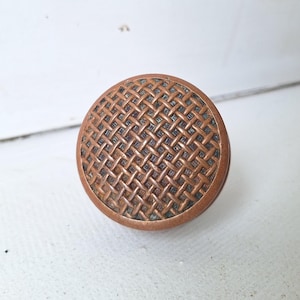 May include: A round, copper-colored cabinet knob with a woven pattern.