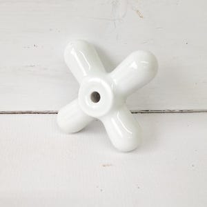 May include: White ceramic cross-shaped knob with a hole in the center.