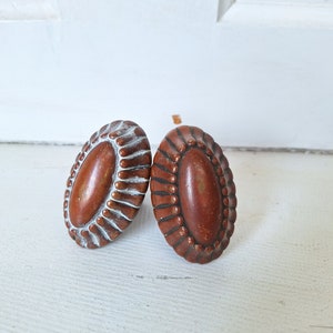 May include: Two oval-shaped brown ceramic drawer pulls with a white painted design. The pulls have a raised, textured edge.
