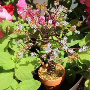 Peut inclure: Une petite sculpture d'arbre en fil de fer avec des perles claires et dorées, en pot dans un pot brun avec des paillettes dorées. L'arbre est entouré de feuilles vertes.