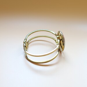 May include: A gold bangle bracelet with a round, colorful, mosaic-style design on the clasp.