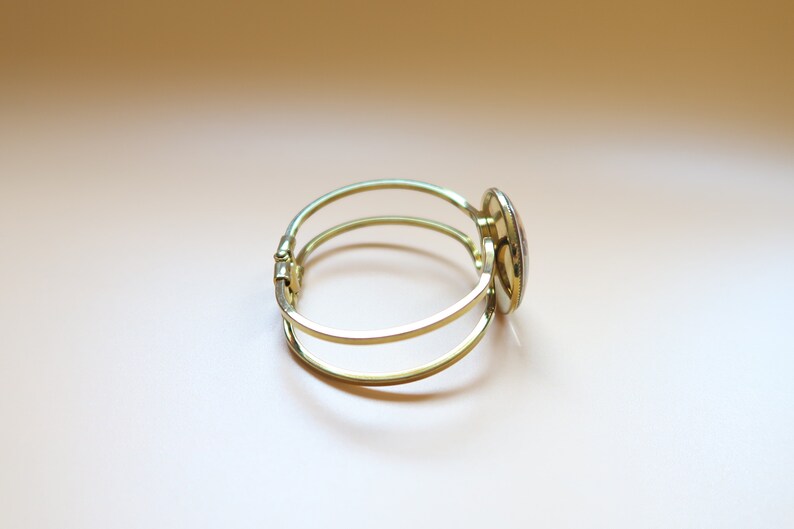 May include: A gold bangle bracelet with a round, colorful, mosaic-style design on the clasp.