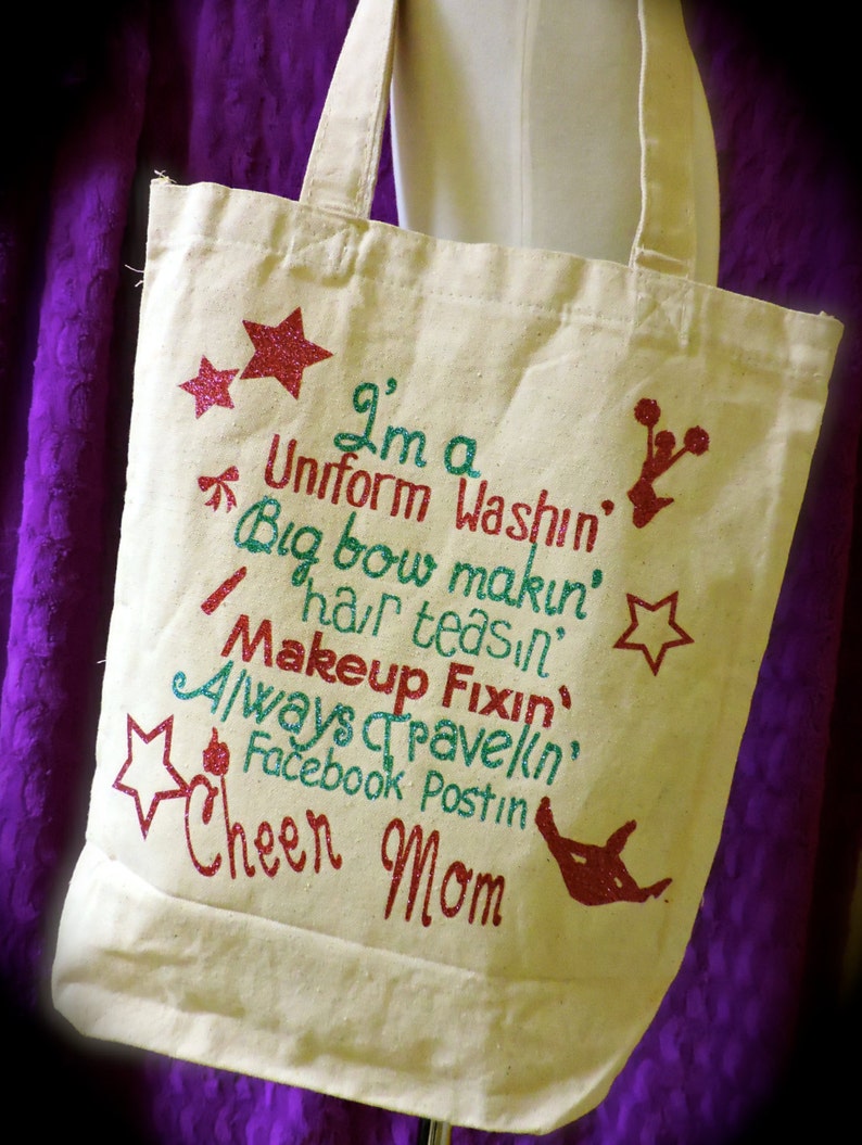 May include: A white canvas tote bag with a glittery design that says "I'm a Uniform Washin', Big bow makin', hair teasin', Makeup Fixin', Always Travelin', Facebook Postin' Cheer Mom".