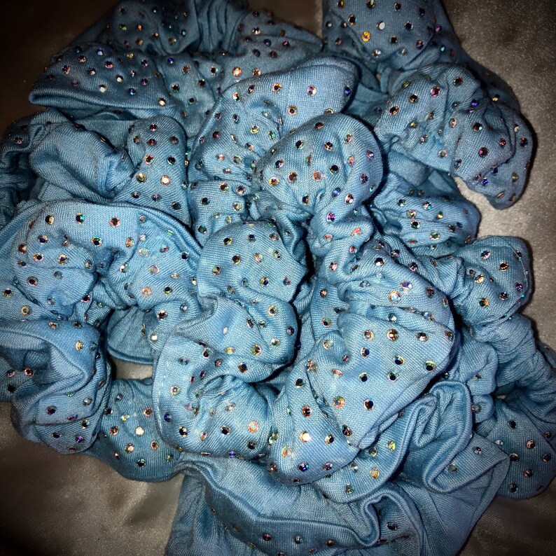 May include: A collection of light blue scrunchies, each adorned with numerous iridescent rhinestones. The scrunchies are made of a soft fabric and are bunched together, creating a textured appearance. The rhinestones sparkle, adding a touch of glamour.