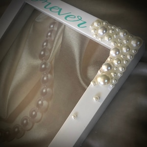 May include: White picture frame with the word "forever" written in teal paint. The frame is decorated with white pearl beads around the edges.