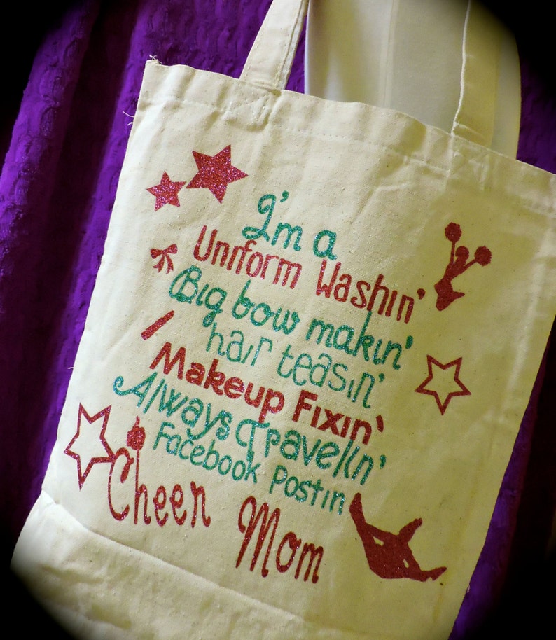 May include: A white canvas tote bag with a glittery design that says "I'm a Uniform Washin', Big Bow Makin', Hair Teas'n, Makeup Fixin', Always Travelin', Facebook Postin' Cheer Mom".