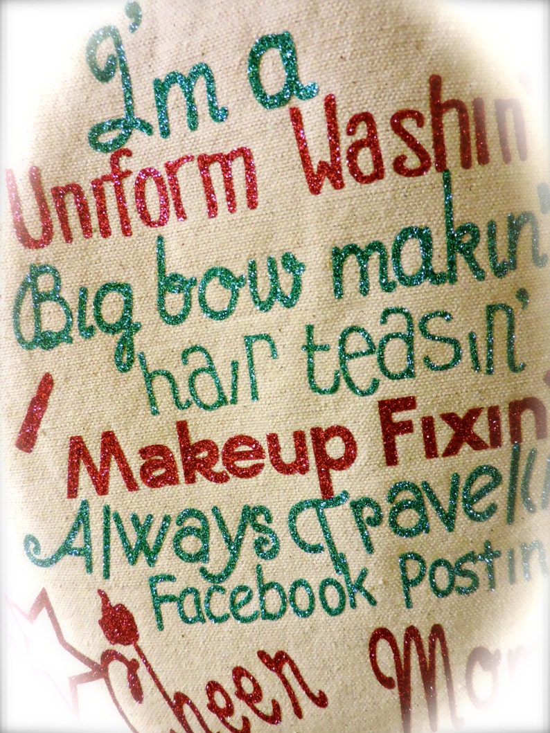 May include: A beige canvas tote bag with the text "I'm a Uniform Washin Big bow makin hair teasin Makeup Fixin Always Travel Facebook Postin" in green and red glitter.