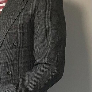 Op de afbeelding: Een grijs dubbelrijig pak met een pinstripe patroon. Het colbert heeft een notch revers en twee knoopsluitingen. De broek van het pak heeft een rechte pijp.
