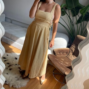 Puede incluir: Un vestido midi amarillo claro con rayas verticales. El vestido presenta un escote cuadrado, tirantes anchos y un corpi&ntilde;o ajustado con cintura fruncida. El vestido tiene una falda fluida y se combina con tacones dorados. El vestido est&aacute; hecho de tela ligera.