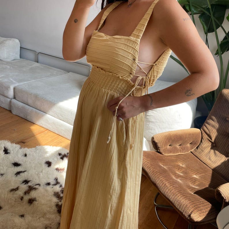 Puede incluir: Vestido largo amarillo claro con corpi&ntilde;o texturizado y falda fluida. El vestido presenta tirantes anchos y un detalle de cordones en los laterales. El vestido est&aacute; confeccionado en tejido ligero, perfecto para el clima c&aacute;lido.