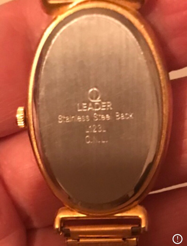 May include: Gold-tone oval watch with a stainless steel back. The watch face is blank and the back of the watch has the text "Leader Stainless Steel Back -123- C.A.L."