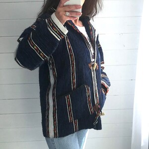 May include: A navy blue hooded jacket with white, red and yellow stripes. The jacket has a toggle closure and two pockets.