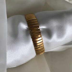 May include: A gold-toned metal bracelet with a flexible, expandable design. The bracelet is made of a series of connected, rectangular links.