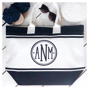 Può includere: Una borsa tote in tela a righe bianche e nere con un monogramma circolare nero che dice "ANM".