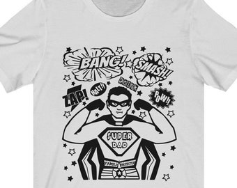 May include: White t-shirt with a black and white illustration of a superhero dad with the text "SUPER DAD" and comic book sound effects like "BANG!" and "SMASH!"