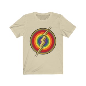May include: A beige t-shirt with a rainbow and lightning bolt design. The design is a stylized version of the Flash logo, with the lightning bolt in the center of a rainbow circle.