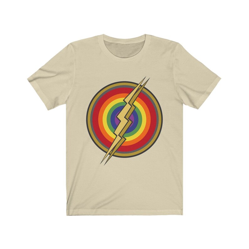 May include: A beige t-shirt with a rainbow and lightning bolt design. The design is a stylized version of the Flash logo, with the lightning bolt in the center of a rainbow circle.