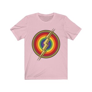 May include: Pink short-sleeved t-shirt with a rainbow and lightning bolt graphic. The graphic is in the center of the shirt and is a stylized version of the Flash logo.