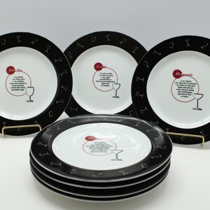 May include: A set of white ceramic plates with black rims featuring cocktail glass silhouettes. Each plate has a recipe in the center, with a red circle and a cocktail glass illustration. The plates are stacked and displayed on a gold stand.