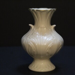 May include: A white porcelain vase with a gold rim and intricate floral designs. The vase has a bulbous body and a flared base.