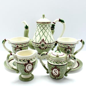 May include: A ceramic tea set with a teapot, cups, creamer, and sugar bowl. The set features a green and white color scheme with a lattice pattern on the teapot and polka dots on the cups. The set includes saucers and is decorated with red accents.