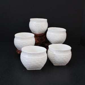 May include: A set of five white ceramic bowls featuring a textured basket-weave pattern on the exterior. Each bowl has a rounded shape with a smooth rim and a slightly tapered base, arranged in a cluster to display the uniform design.
