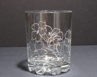May include: A clear glass tumbler with a floral design etched into the side. The flowers are white and appear to be a type of hibiscus.