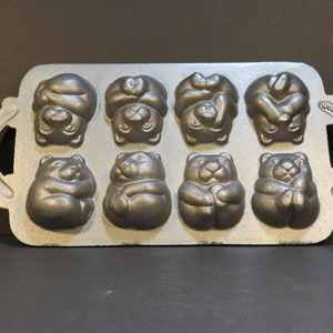 May include: A cast iron baking pan with eight bear-shaped molds. The pan is gray and has two handles.